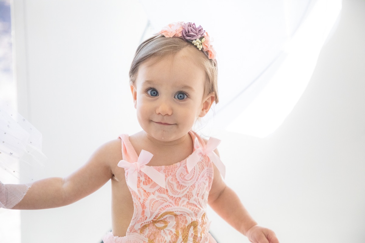 Little girl in a pink birthday dress beside a bright window