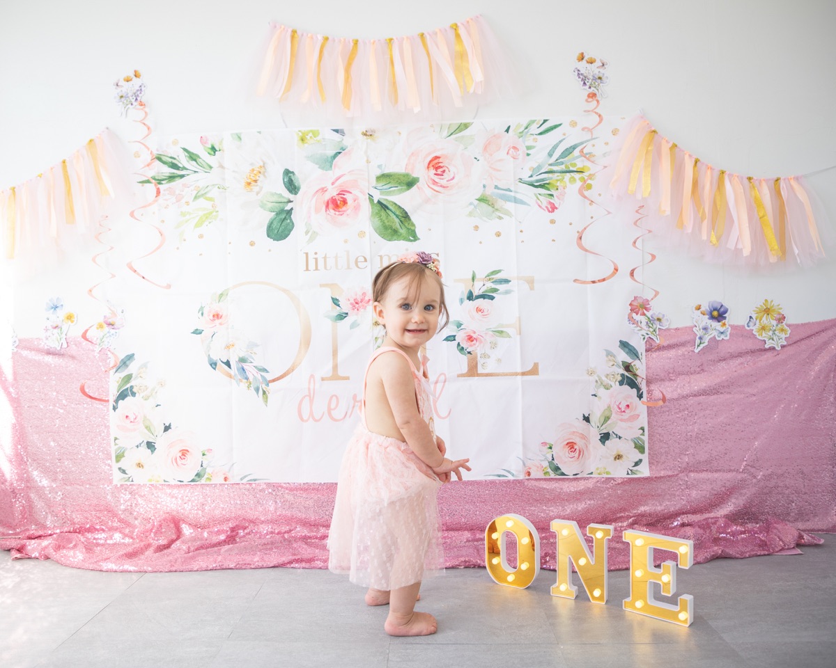 Birthday girl with the complete floral backdrop, pink decorations, and illuminated ONE letters