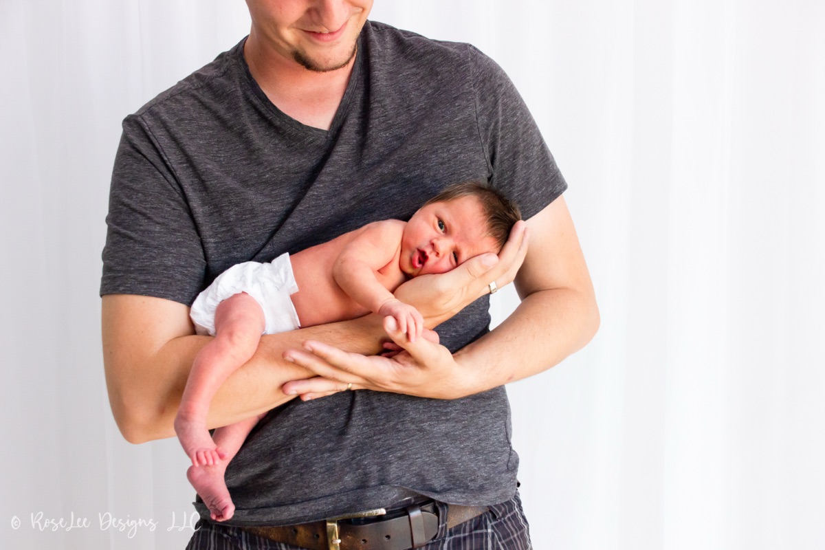 Newborn cradled in an adult’s hands against a soft white background