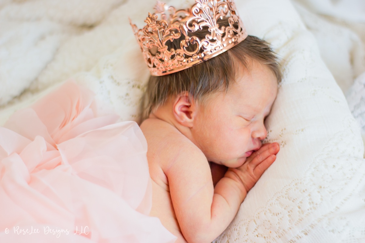 Sleeping newborn wearing a tiny crown and a soft pink wrap