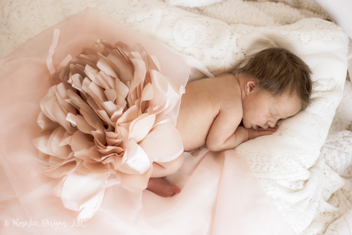 Sleeping newborn curled beside a large soft pink flower
