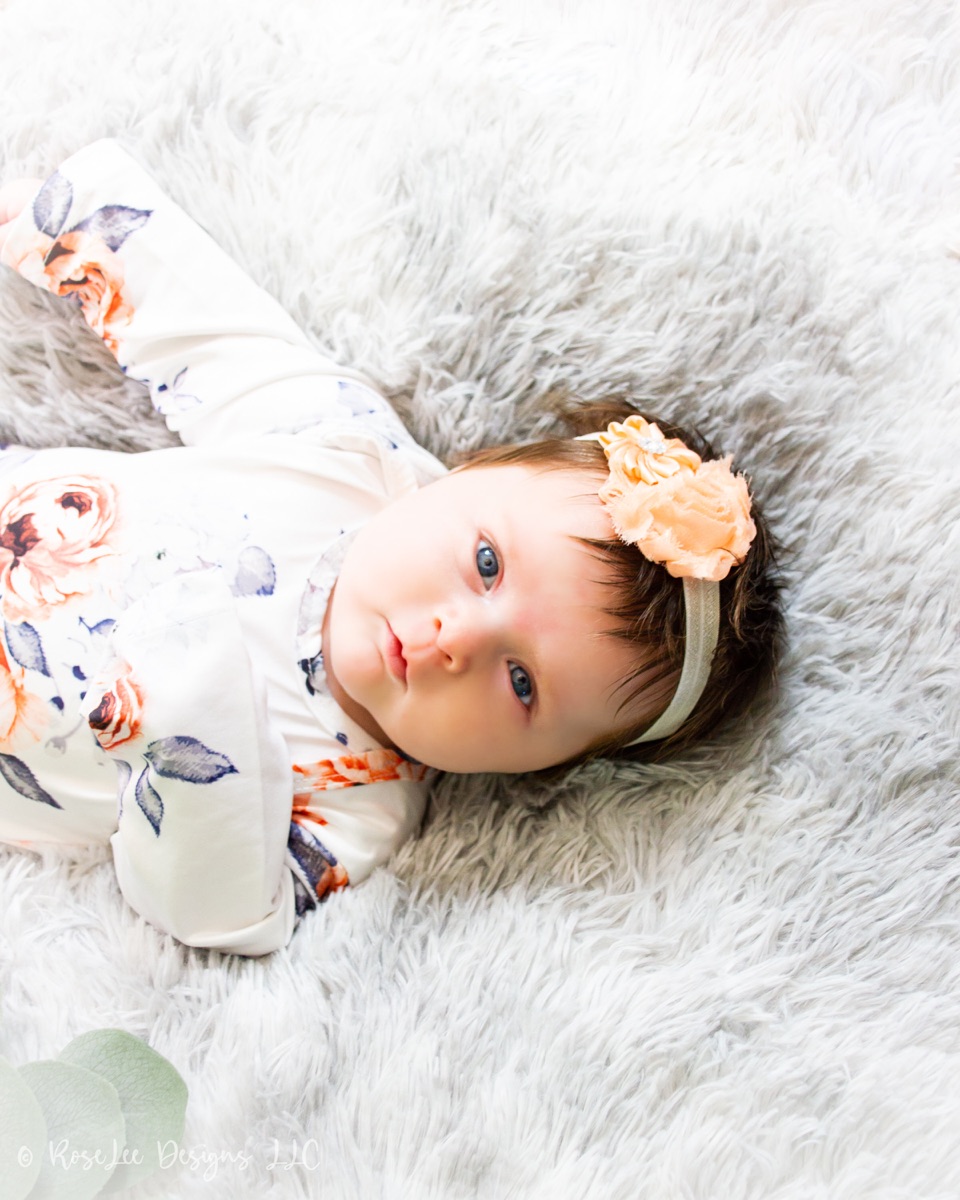 Baby surrounded by soft flowers on a white blanket