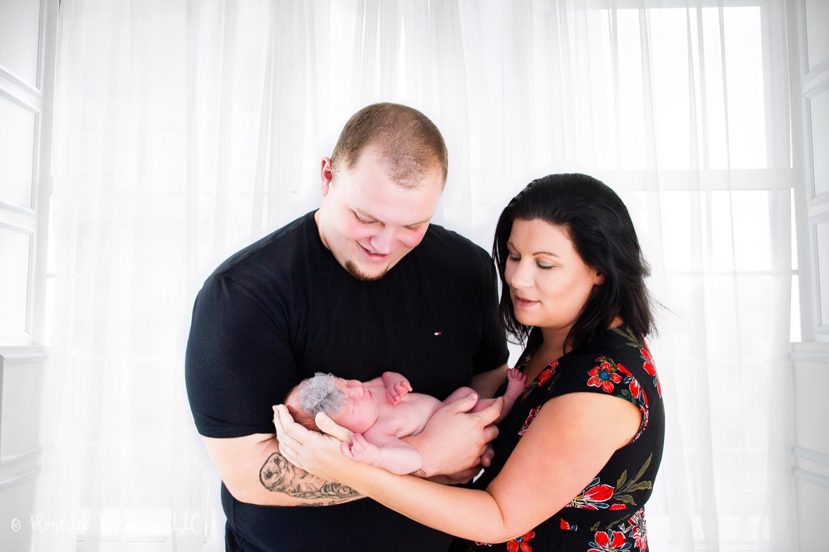 Parents looking down at their newborn beside a bright window
