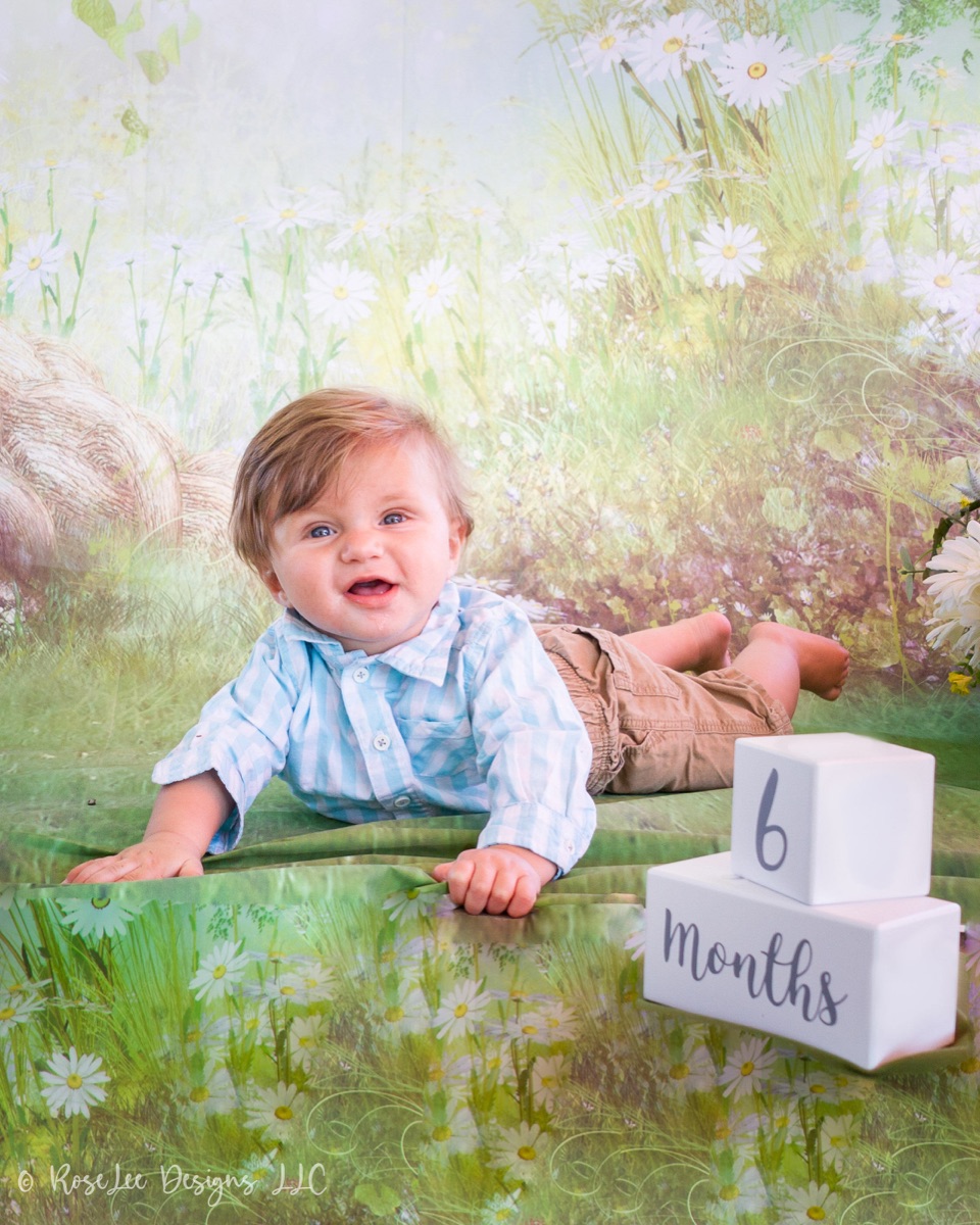 Smiling baby boy in pale blue sitting among soft spring flowers