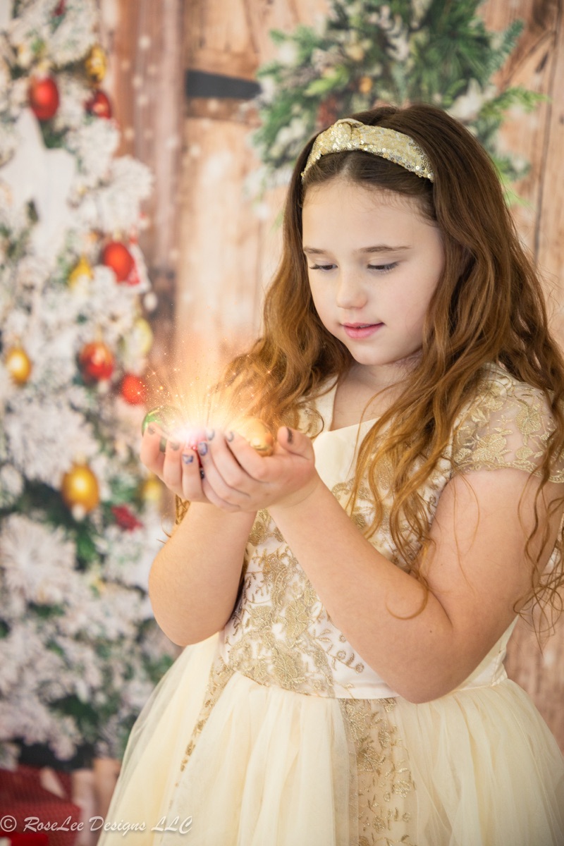 Girl in a gold dress holding a glowing light in a Christmas portrait