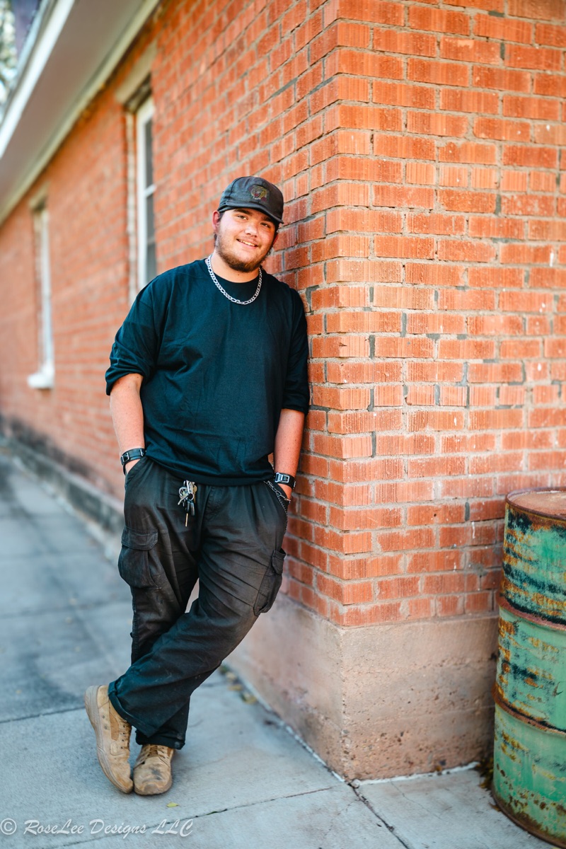Young man in a black cap leaning against a red brick wall