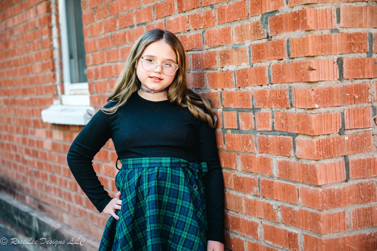Young woman in a green plaid skirt beside a red brick wall