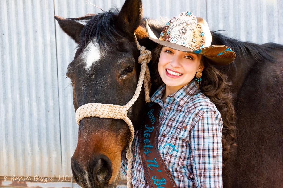 Smiling young woman in a cowboy hat beside her black horse