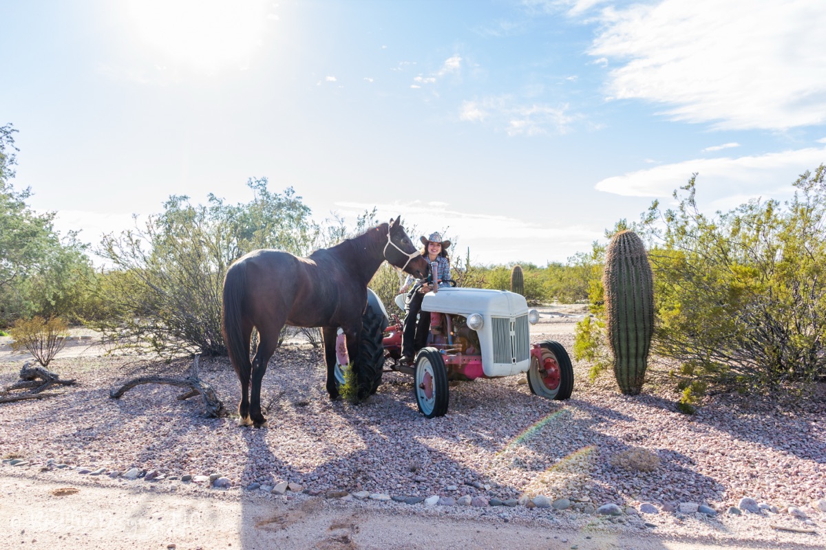 Young woman with her horse beside a vintage tractor in the desert
