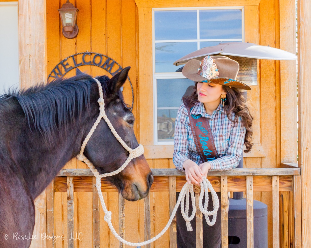 Young woman in a cowboy hat with her horse beside a wooden stable