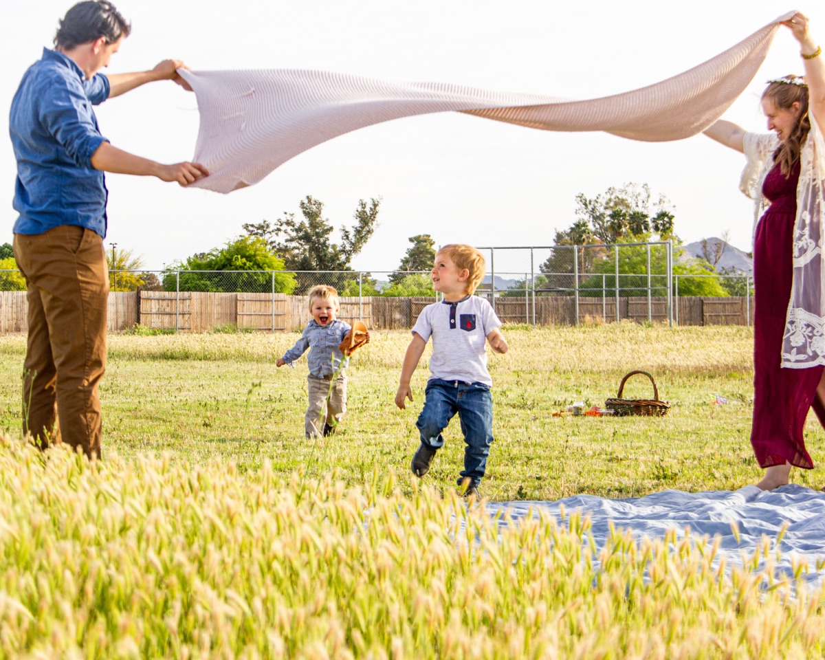 Parents lifting a blanket as their children run beneath it in a sunny field