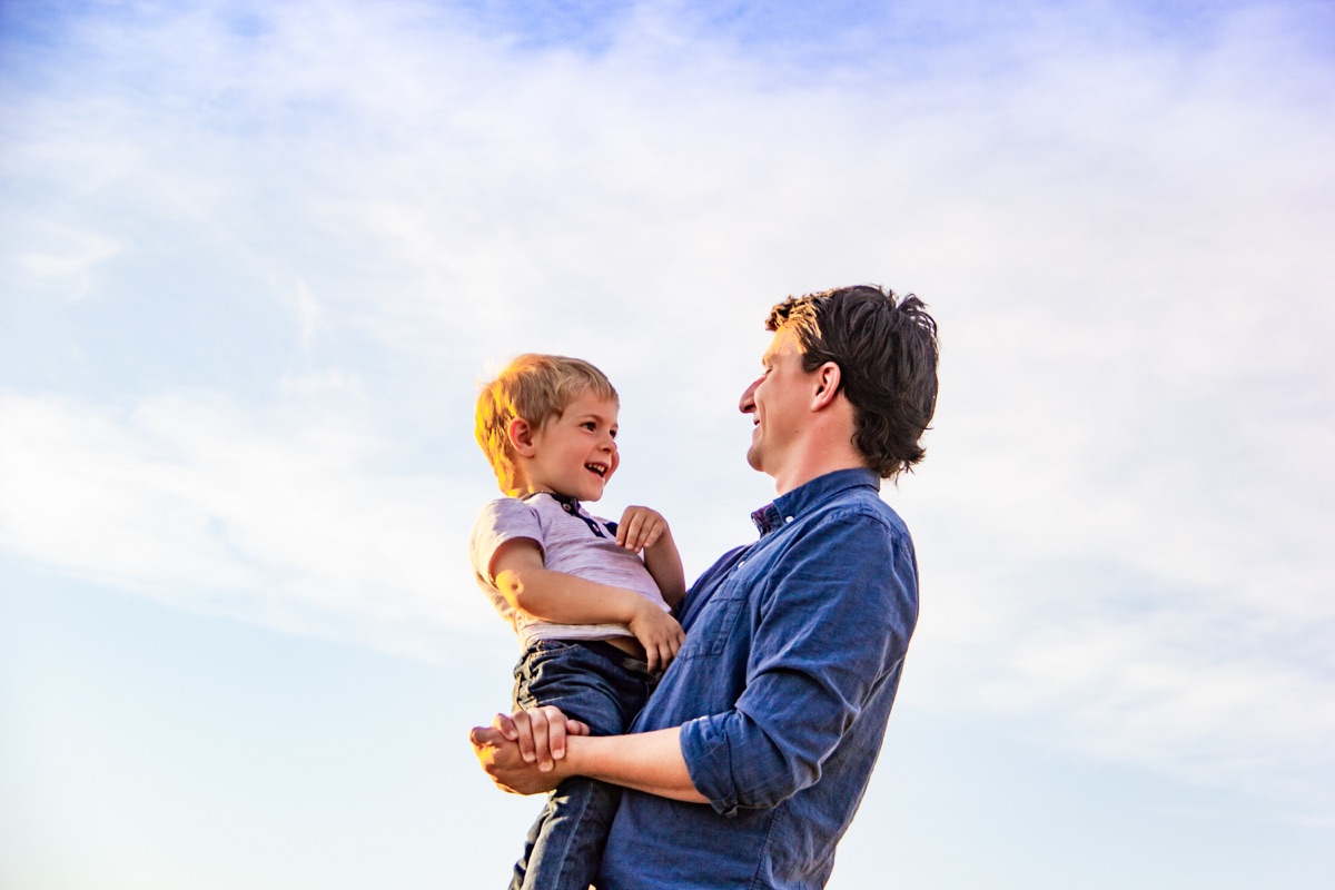 Father holding his laughing little boy beneath a bright open sky