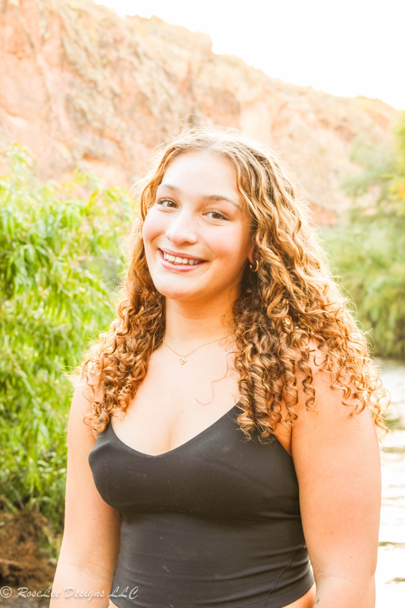 Young woman smiling beside a river surrounded by soft green trees