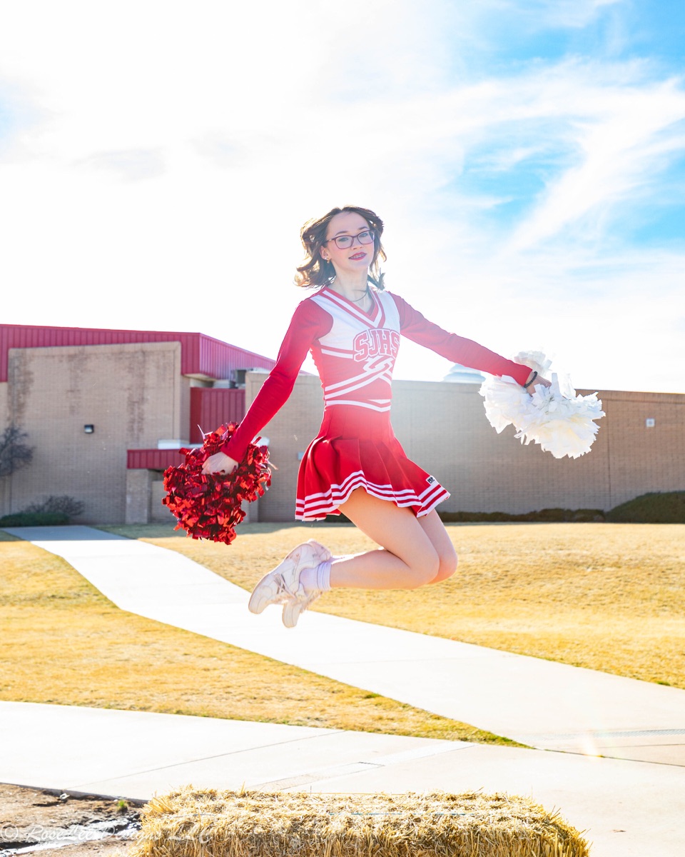 Cheerleader jumping in the sunshine beside stadium bleachers