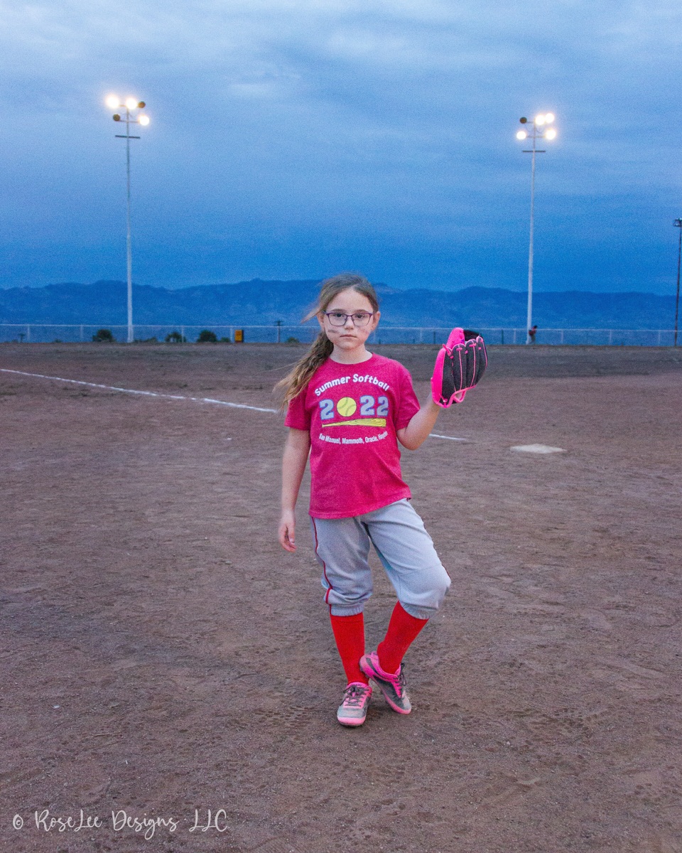 Softball player beneath stadium lights at blue hour