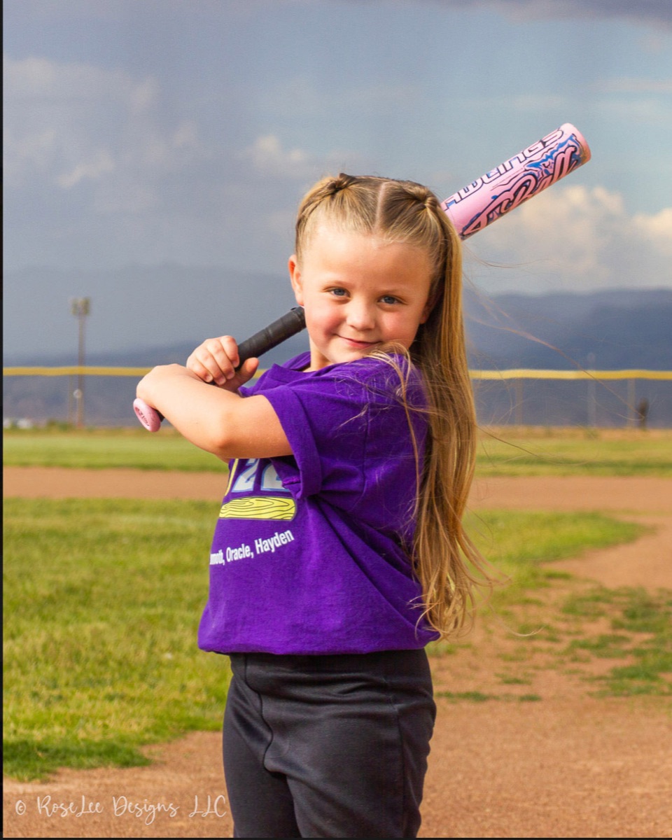 Young softball player in purple smiling with her bat