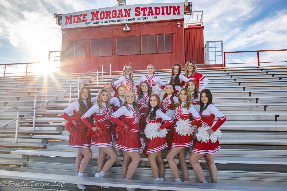 Cheerleading team posing together on sunlit stadium bleachers