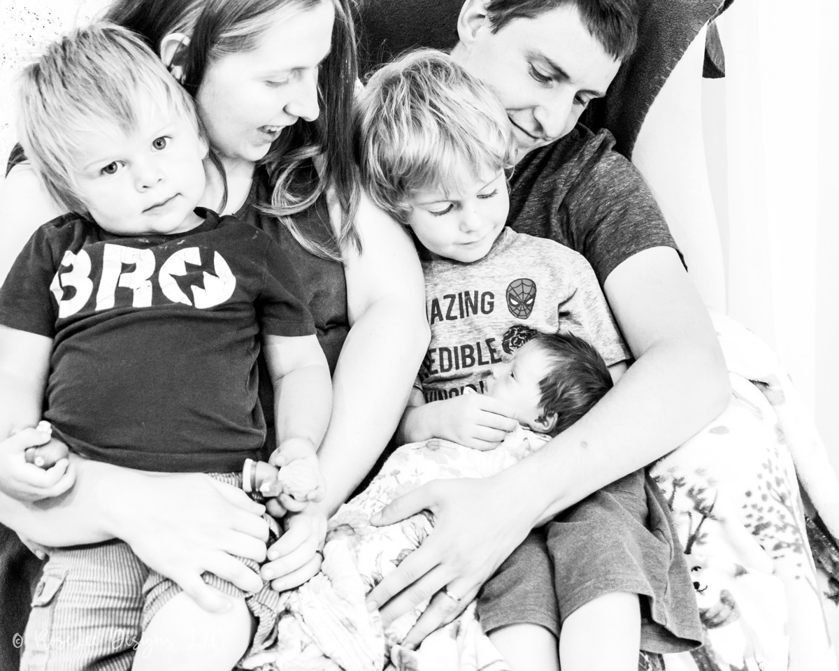 Parents cuddling their two young children in black and white
