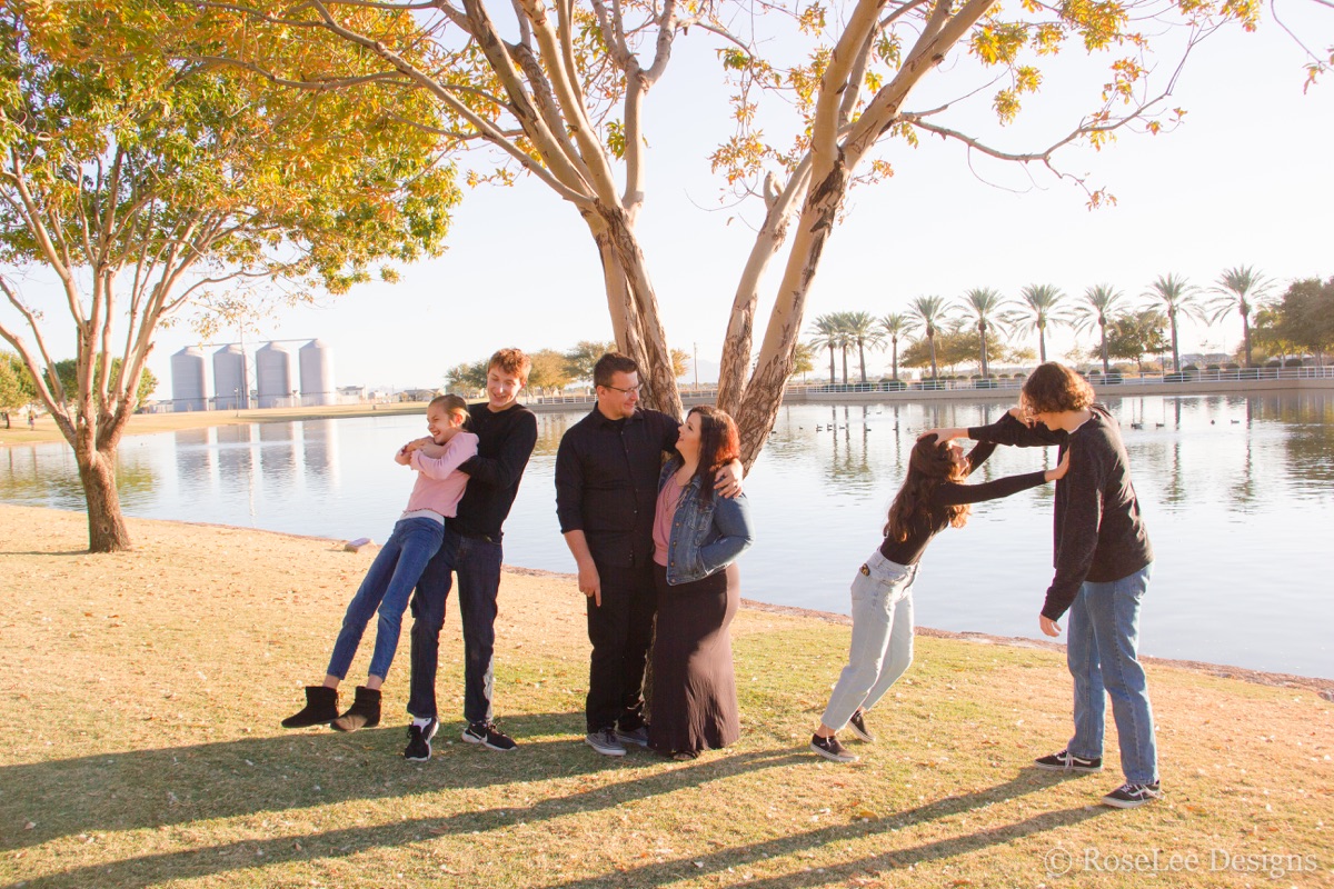 Family holding hands beneath a tree beside the water
