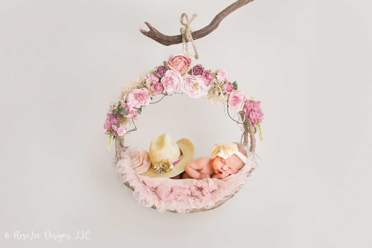 Sleeping newborn nestled inside a floral wreath hanging from a branch