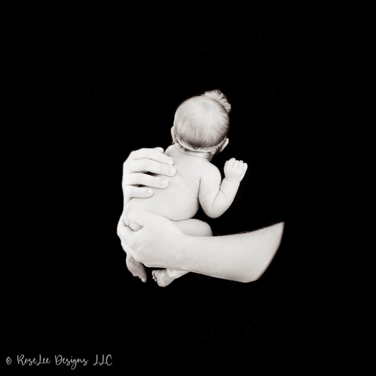 Tiny newborn resting in an adult hand against a black background