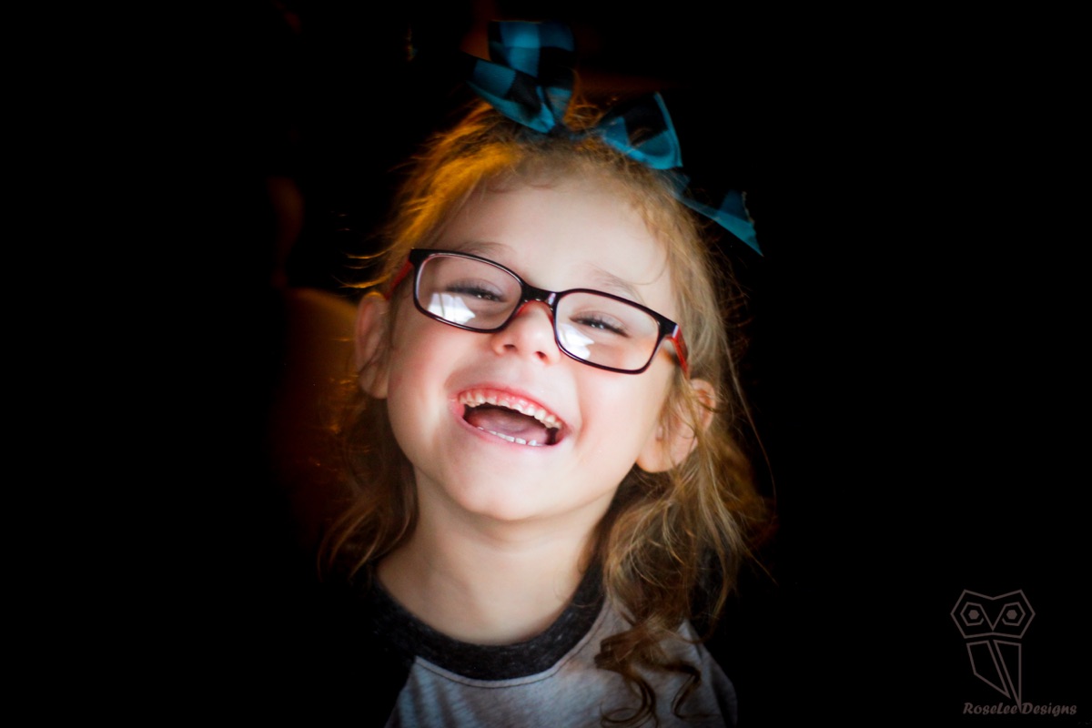 Laughing young girl wearing glasses against a dark background