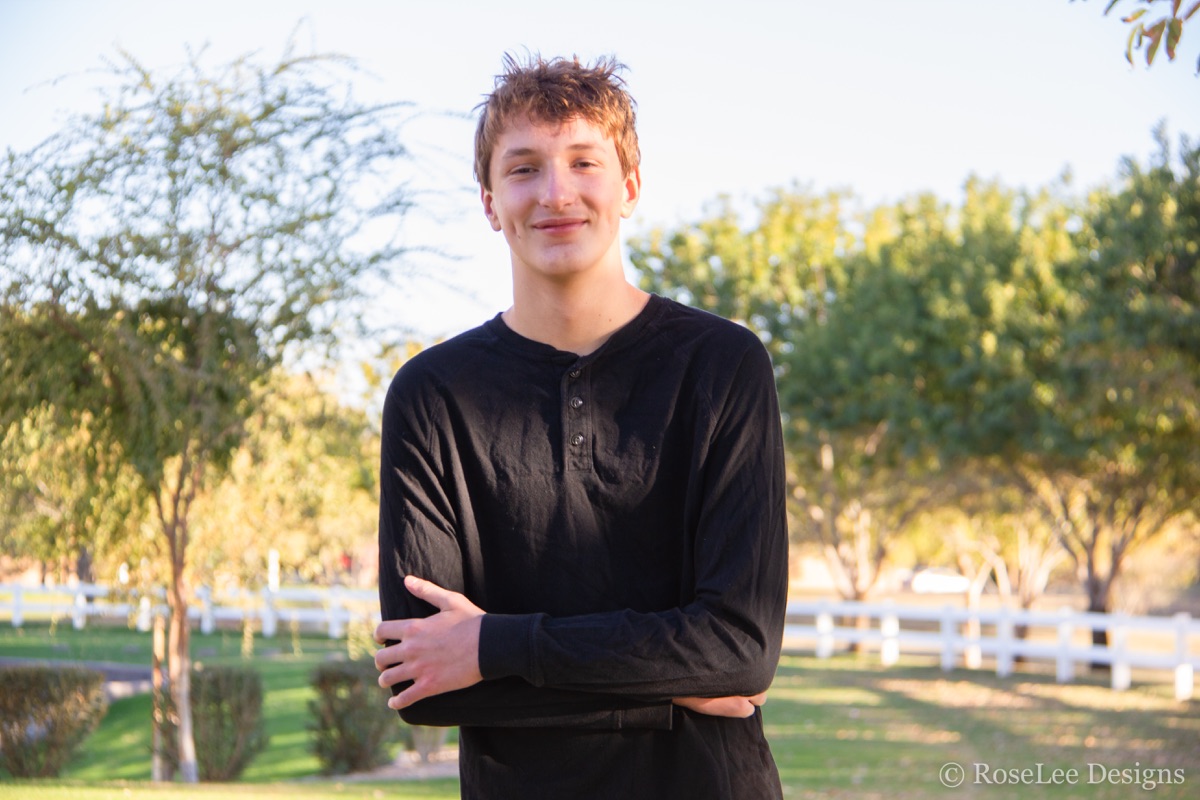 Young man with folded arms beneath green trees