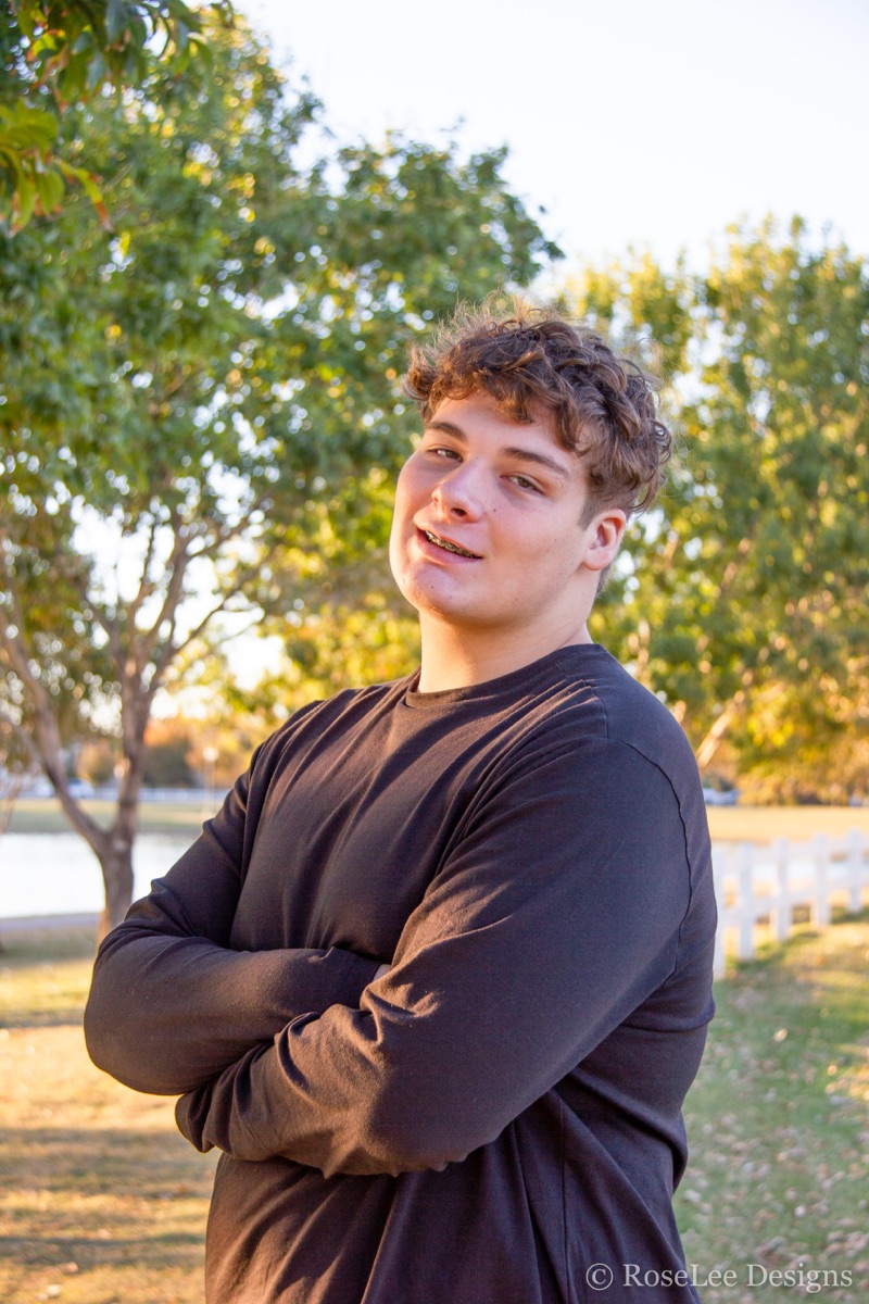 Young man in a brown shirt beneath warm sunlit trees