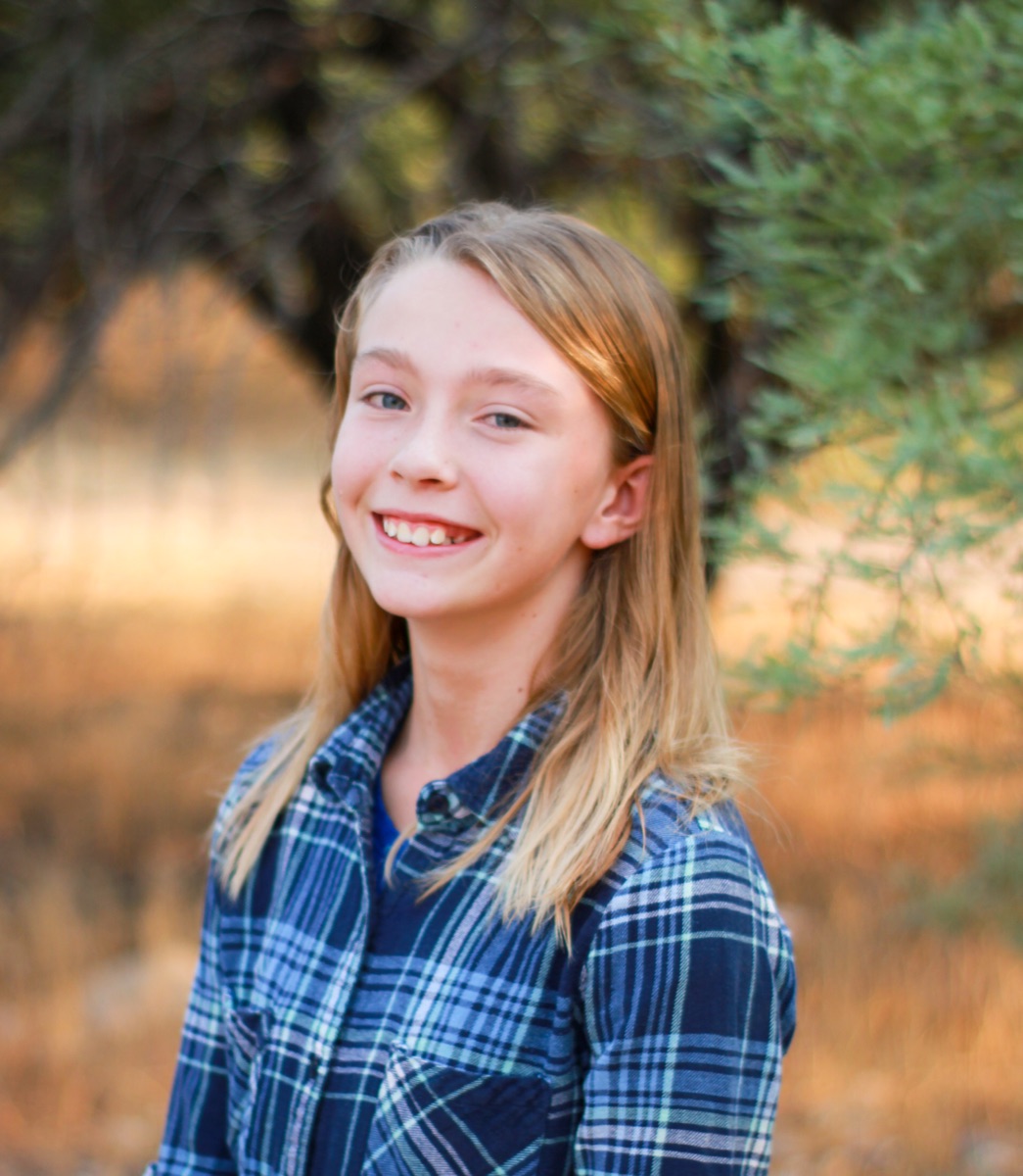Smiling young girl in a blue plaid shirt beneath autumn trees