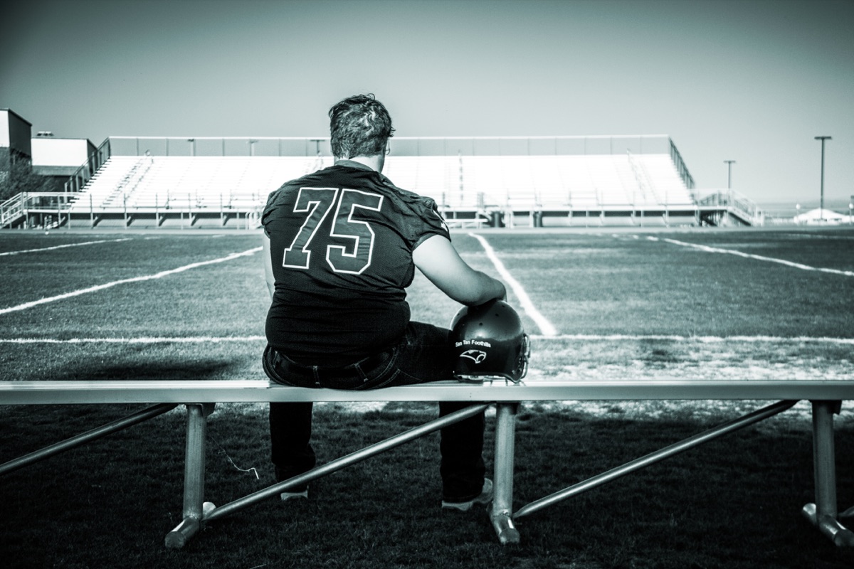 Football player seated in an empty stadium, photographed in black and white