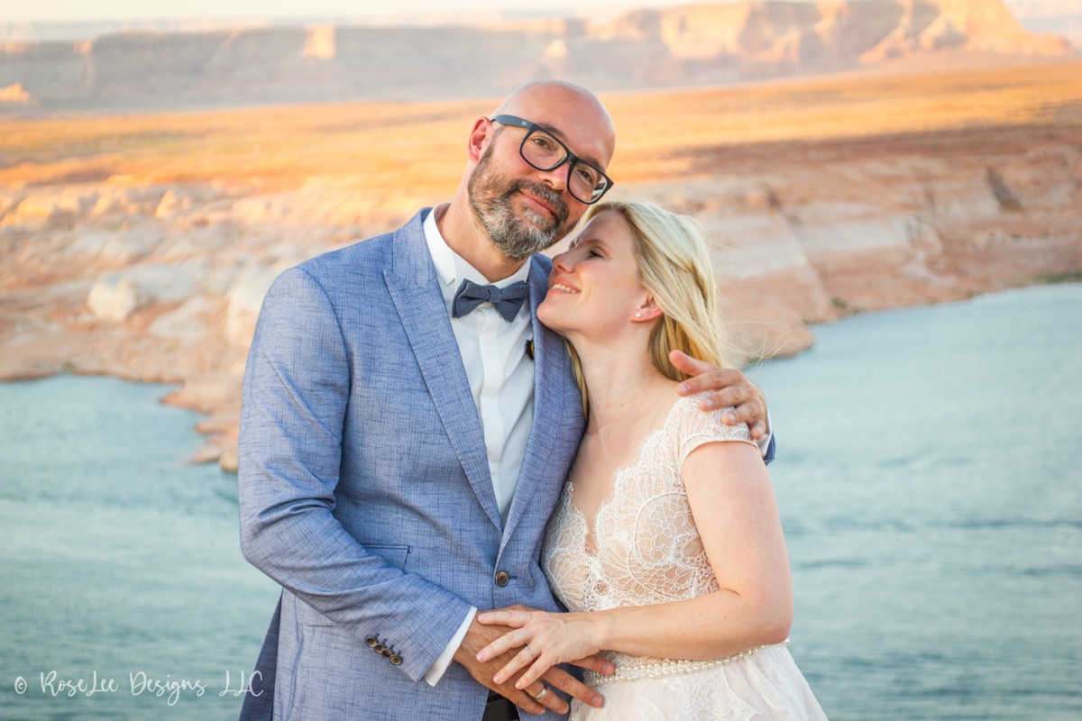 Newlyweds leaning close together above a desert lake