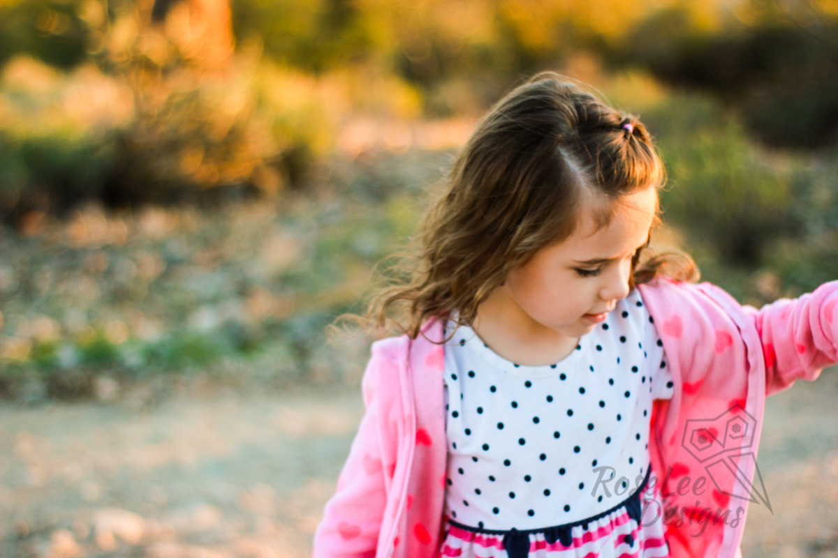 Little girl in a pink cardigan and polka-dot dress beneath autumn trees