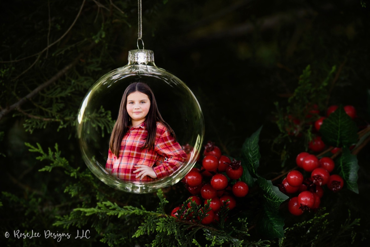 Creative Christmas portrait of a girl inside a glass ornament among evergreen branches