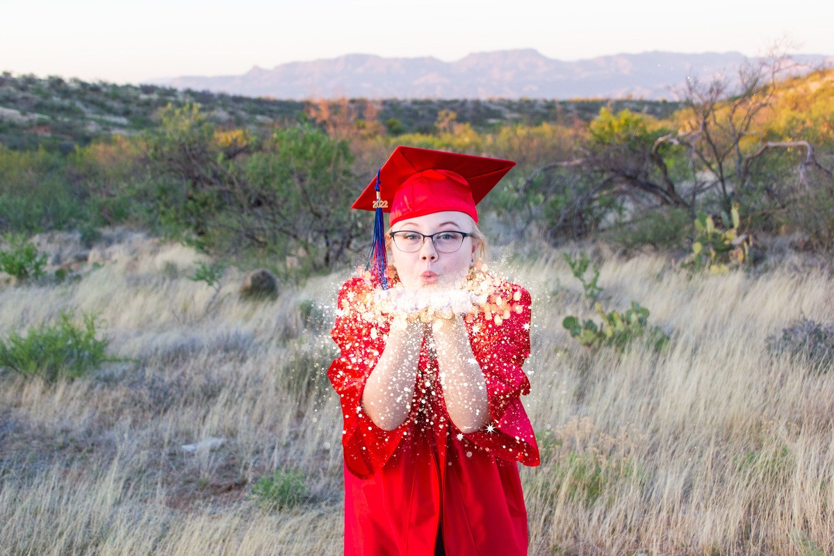 Graduate in a red cap and gown holding a jar of glowing lights