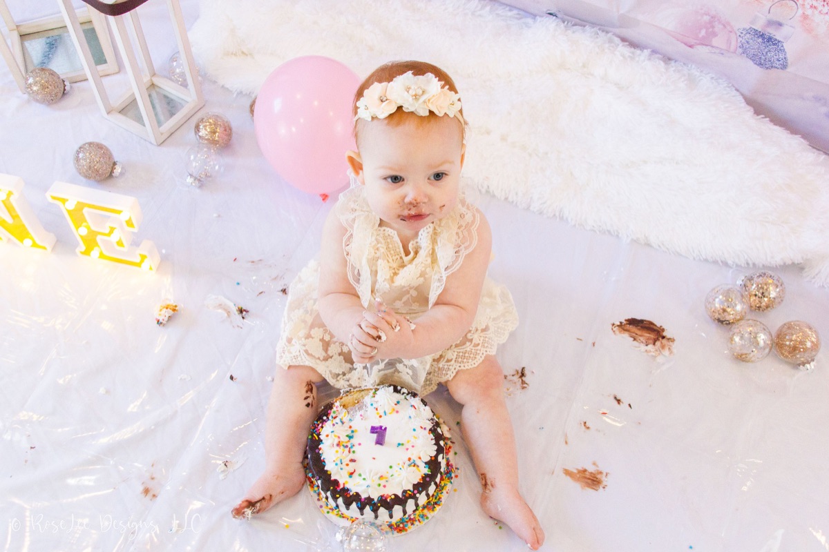 Baby in a pink birthday outfit tasting cake frosting