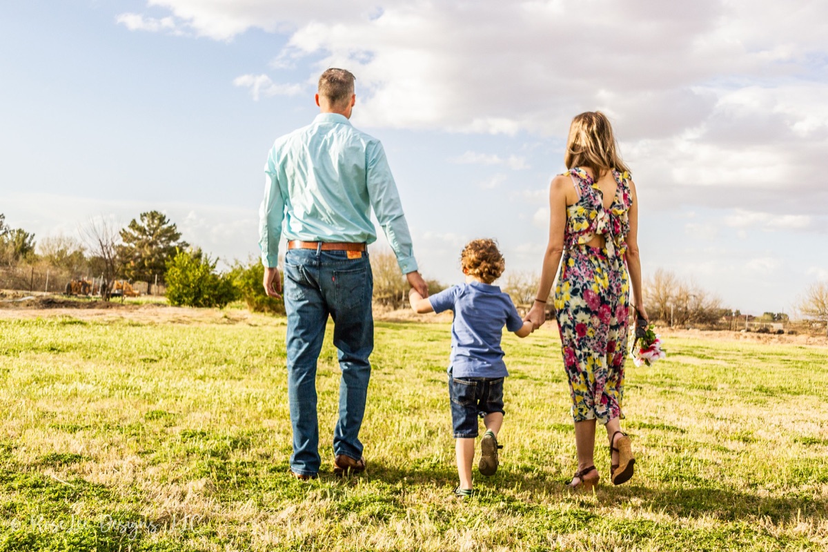 Parents walking hand in hand with their little boy beneath a cloud-filled sky