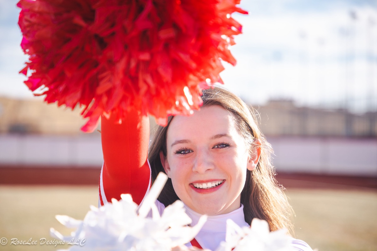 Smiling cheerleader beneath a bright red pom-pom