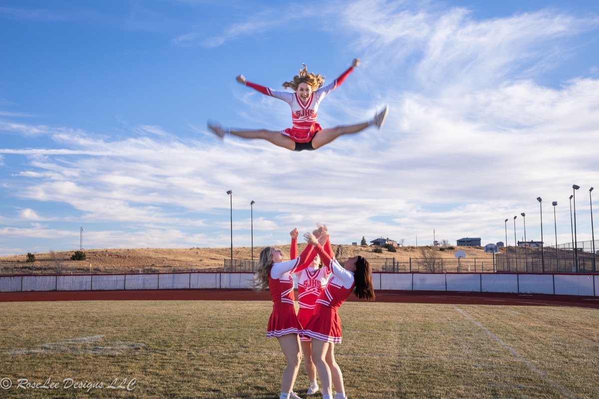 Cheerleading teammates performing a high aerial stunt beneath a blue sky